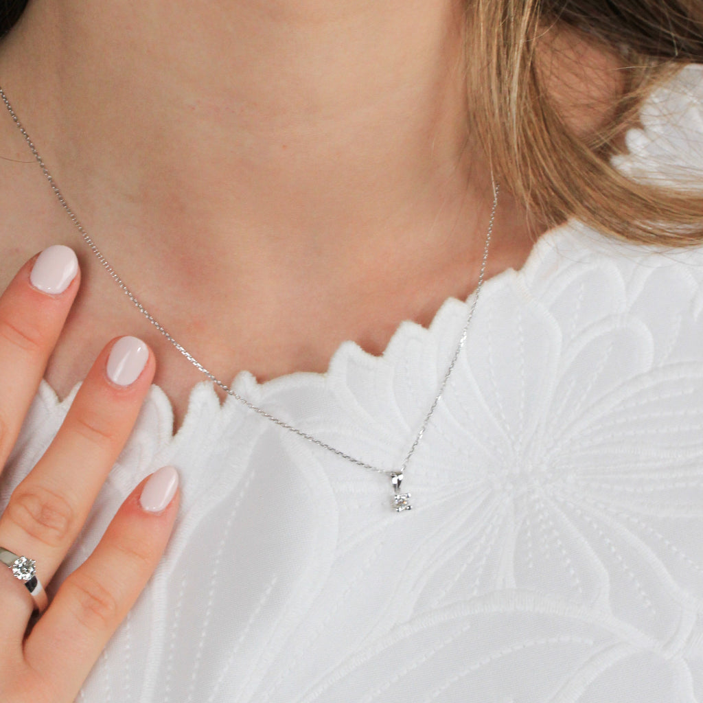 Colgante en oro blanco de 18 quilates con un solitario de diamante de engarzado en cuatro garras cuadradas. Anilla triangular. Joyería Pamplona.