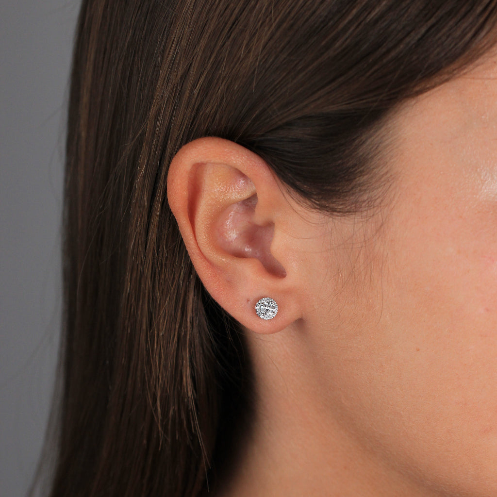 Pendientes de oro blanco de 18k con un diamante solitario engastado en cuatro garras y una orla de diamantes