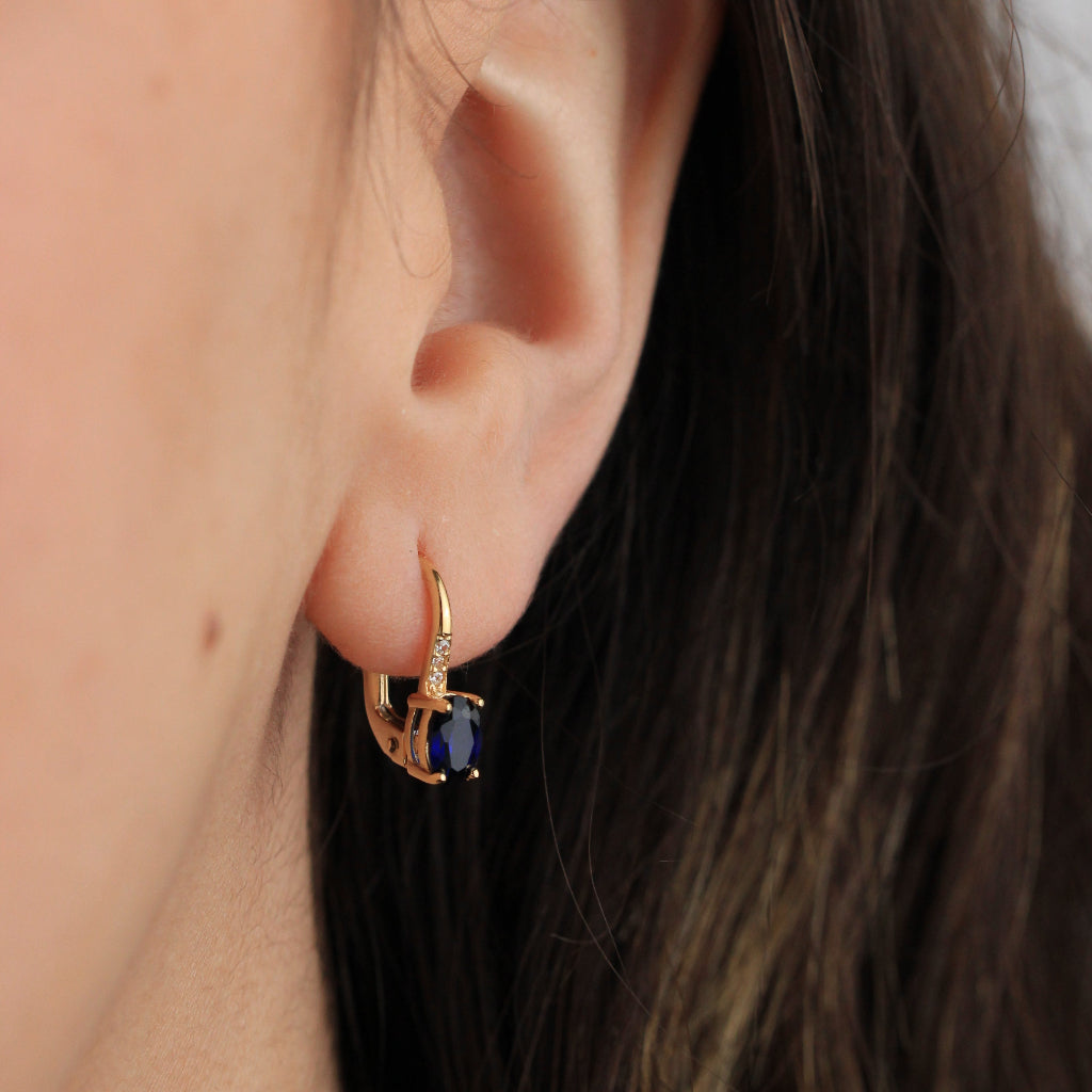 Pendientes en oro amarillo de 18 quilates con una zafiro talla oval en garras y tres circonitas.