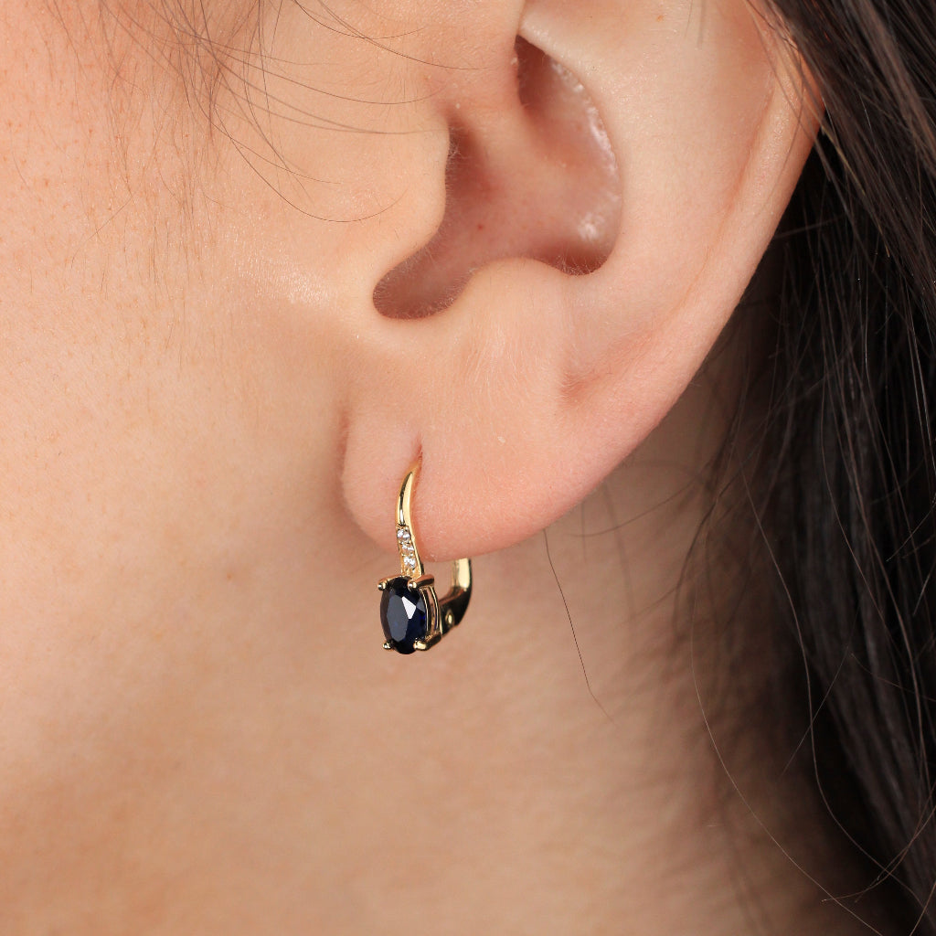 Pendientes en oro amarillo de 18 quilates con una zafiro talla oval en garras y tres circonitas.