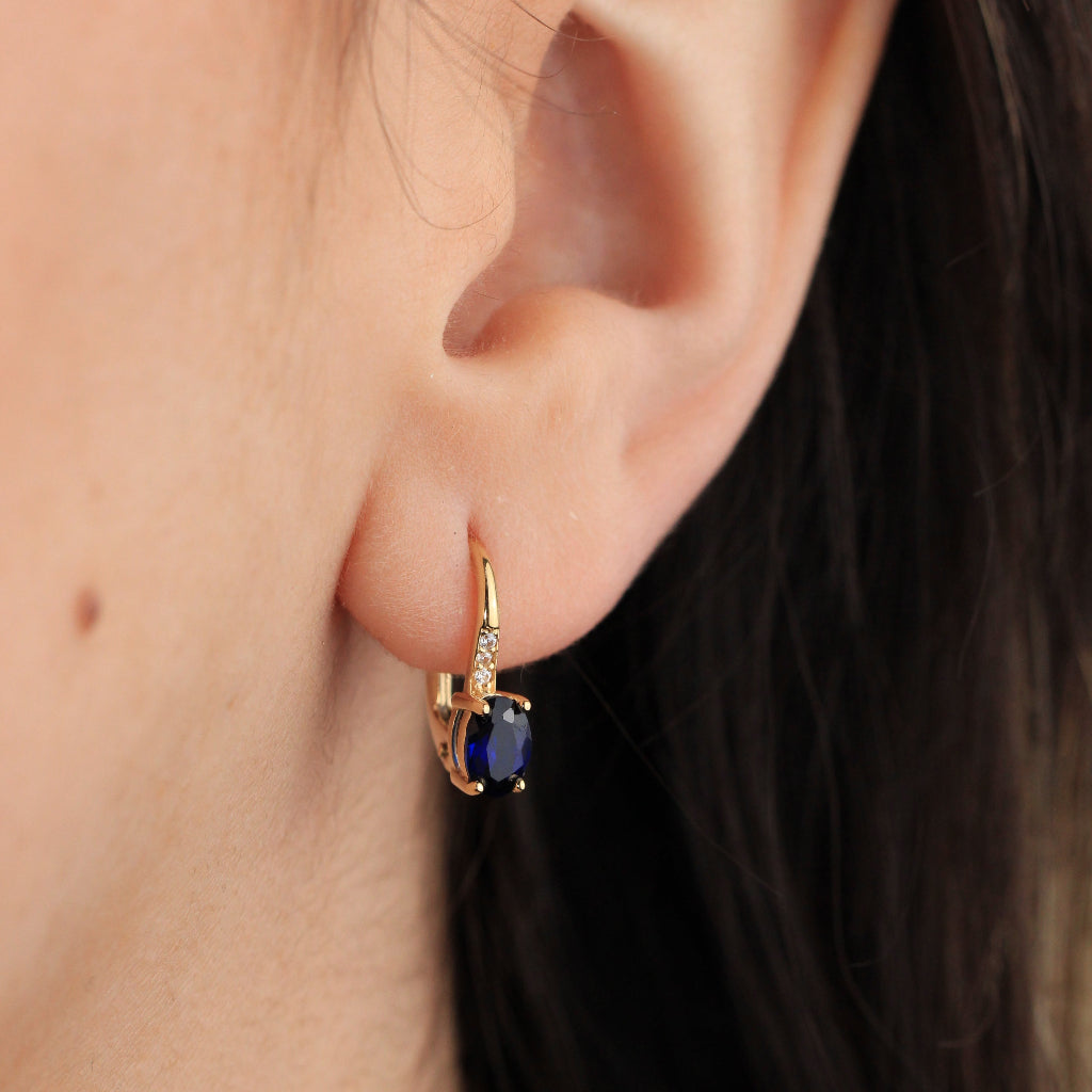 Pendientes en oro amarillo de 18 quilates con una zafiro talla oval en garras y tres circonitas.