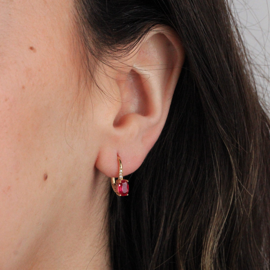 Pendientes en oro amarillo de 18 quilates con una rubí talla oval en garras y tres circonitas.