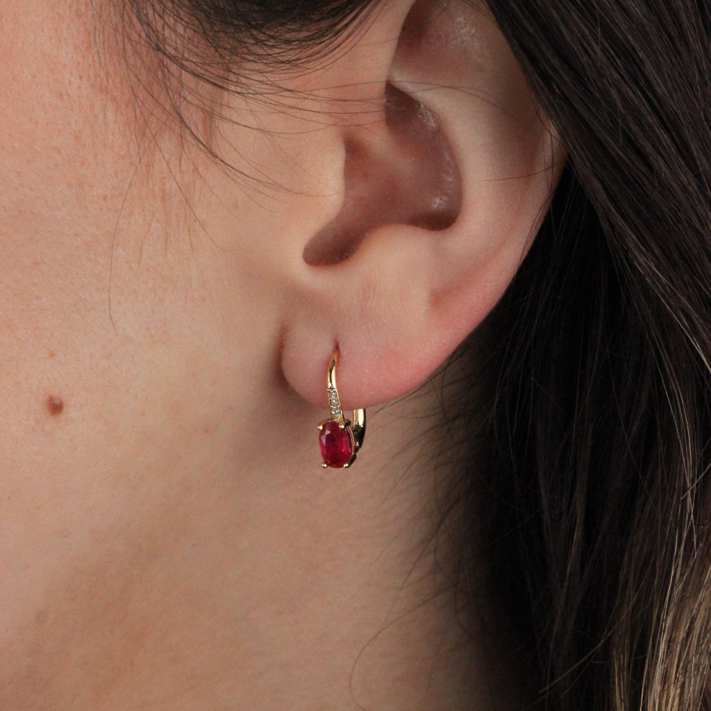 Pendientes en oro amarillo de 18 quilates con una rubí talla oval en garras y tres circonitas.