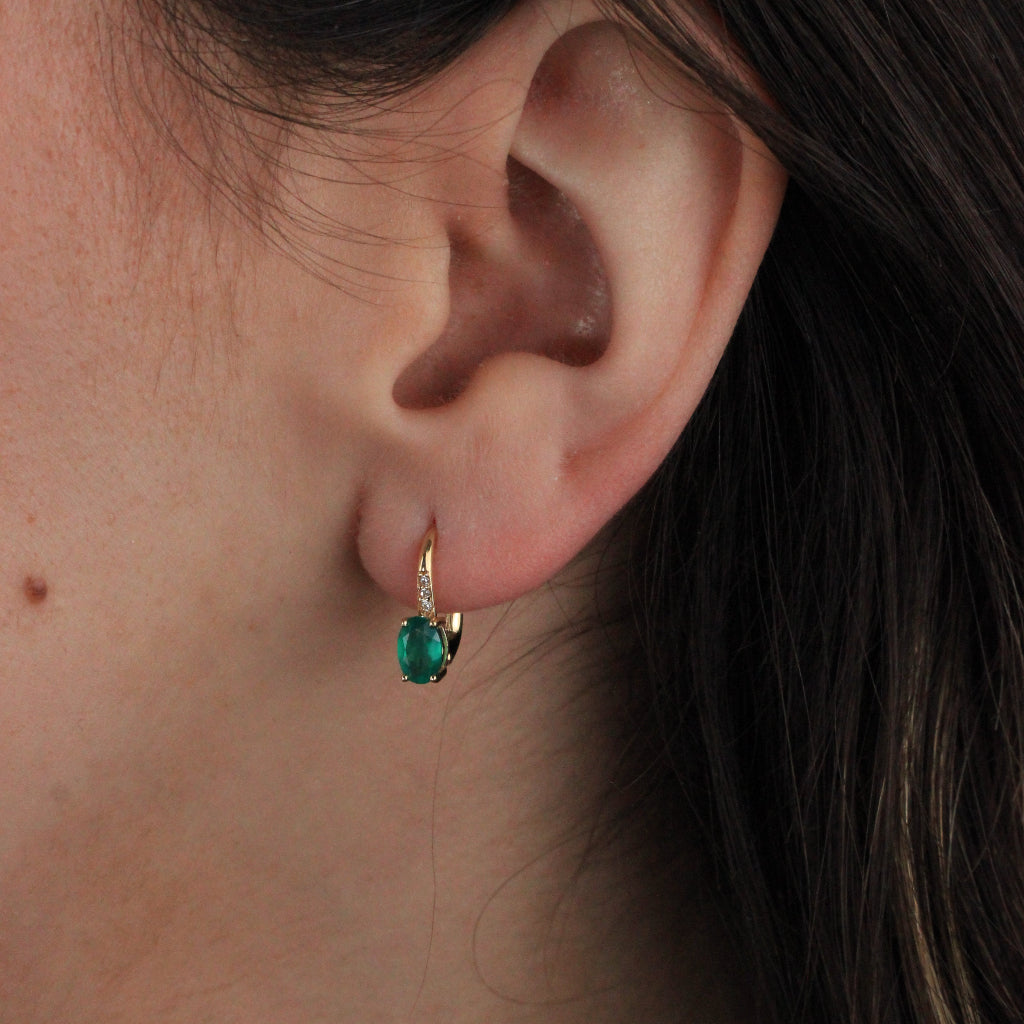 Pendientes en oro amarillo de 18 quilates con una esmeralda talla oval en garras y tres circonitas.