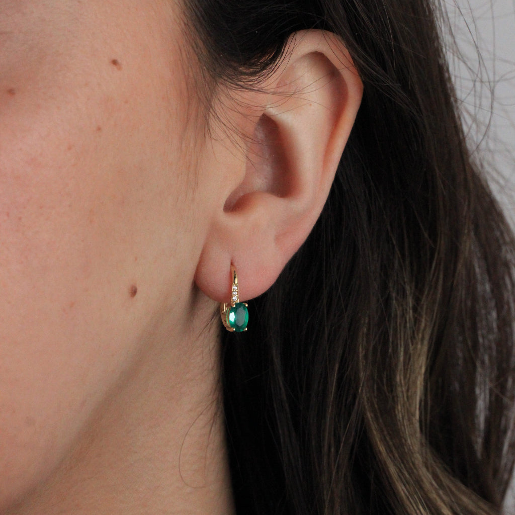 Pendientes en oro amarillo de 18 quilates con una esmeralda talla oval en garras y tres circonitas.