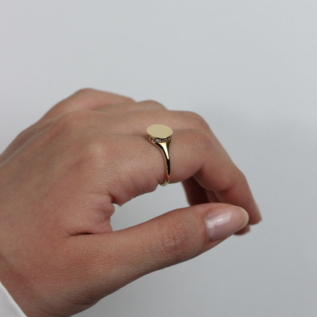 Sello para niña circular realizado en oro amarillo de 18 quilates y una orla de circonitas en altura.