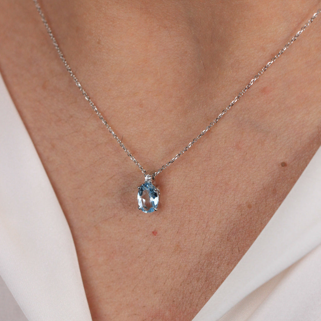 Collar en oro blanco de 18 quilates con un colgante de topacio azul talla oval en garras y una circonita.