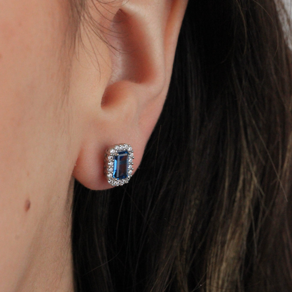 Pendientes de oro blanco de 18 quilates con una circonita azul con orla de circonitas incoloras.