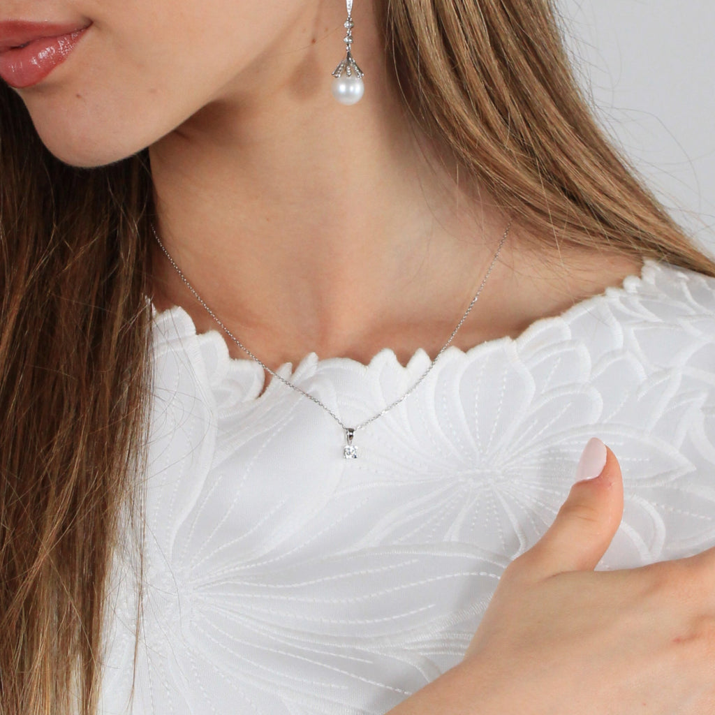 Colgante en oro blanco de 18 quilates con un solitario de diamante de engarzado en cuatro garras cuadradas. Anilla triangular. Joyería Pamplona.