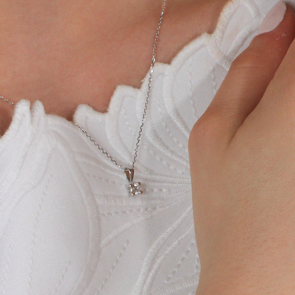 Colgante en oro blanco de 18 quilates con un solitario de diamante de engarzado en cuatro garras cuadradas. Anilla triangular. Joyería Pamplona.