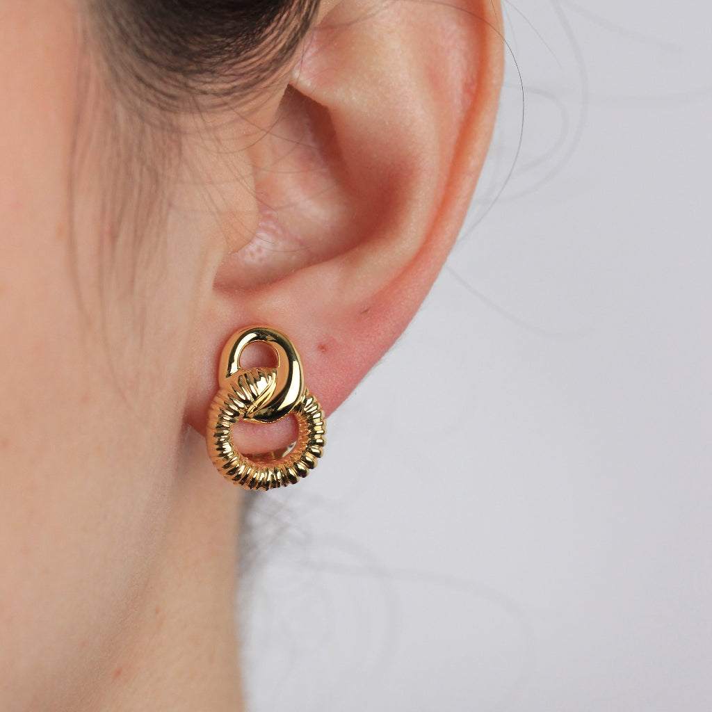 Pendientes en oro amarillo de 18 quilates con dos aros enlazados en forma de ocho. El aro inferior está facetado. Sistema de cierre omega.