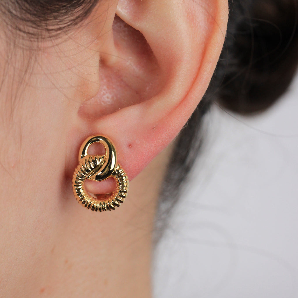 Pendientes en oro amarillo de 18 quilates con dos aros enlazados en forma de ocho. El aro inferior está facetado. Sistema de cierre omega.