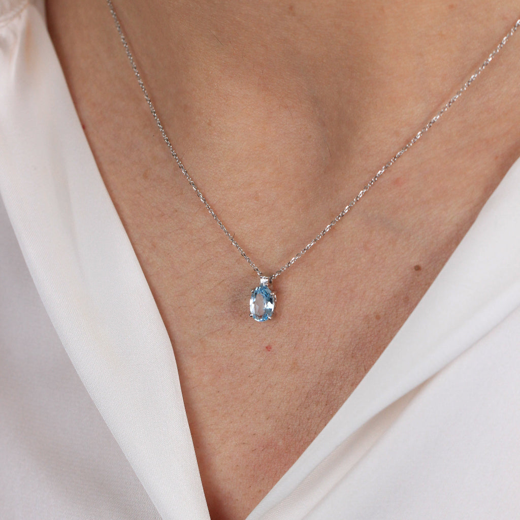 Collar en oro blanco de 18 quilates con un colgante de topacio azul talla oval en garras y una circonita.