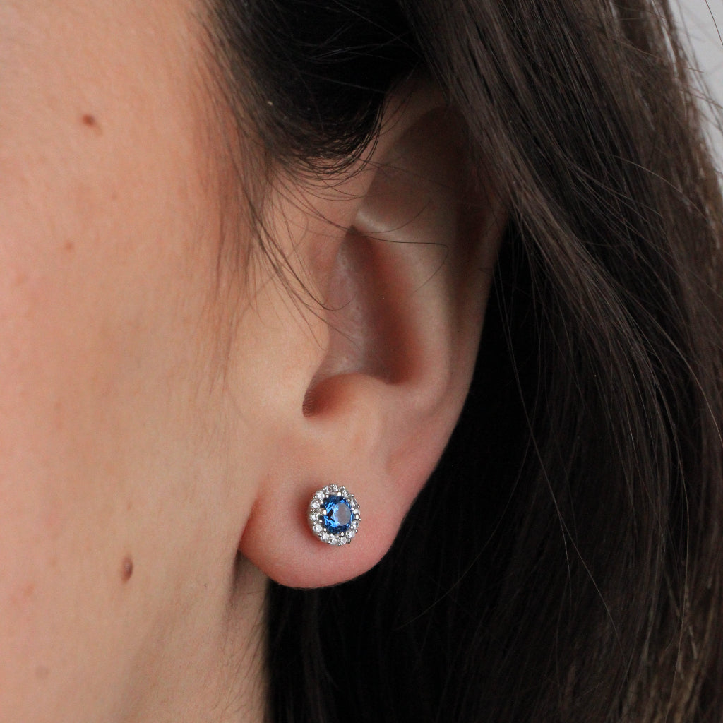 Pendientes en oro blanco de 18 quilates con un circonita azul con orla de circonitas incoloras.