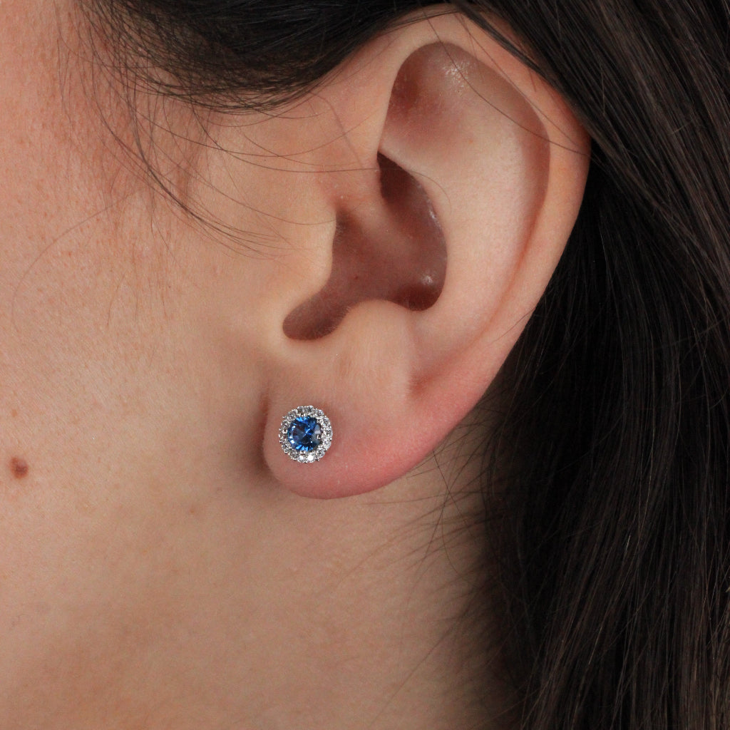 Pendientes en oro blanco de 18 quilates con un circonita azul con orla de circonitas incoloras.