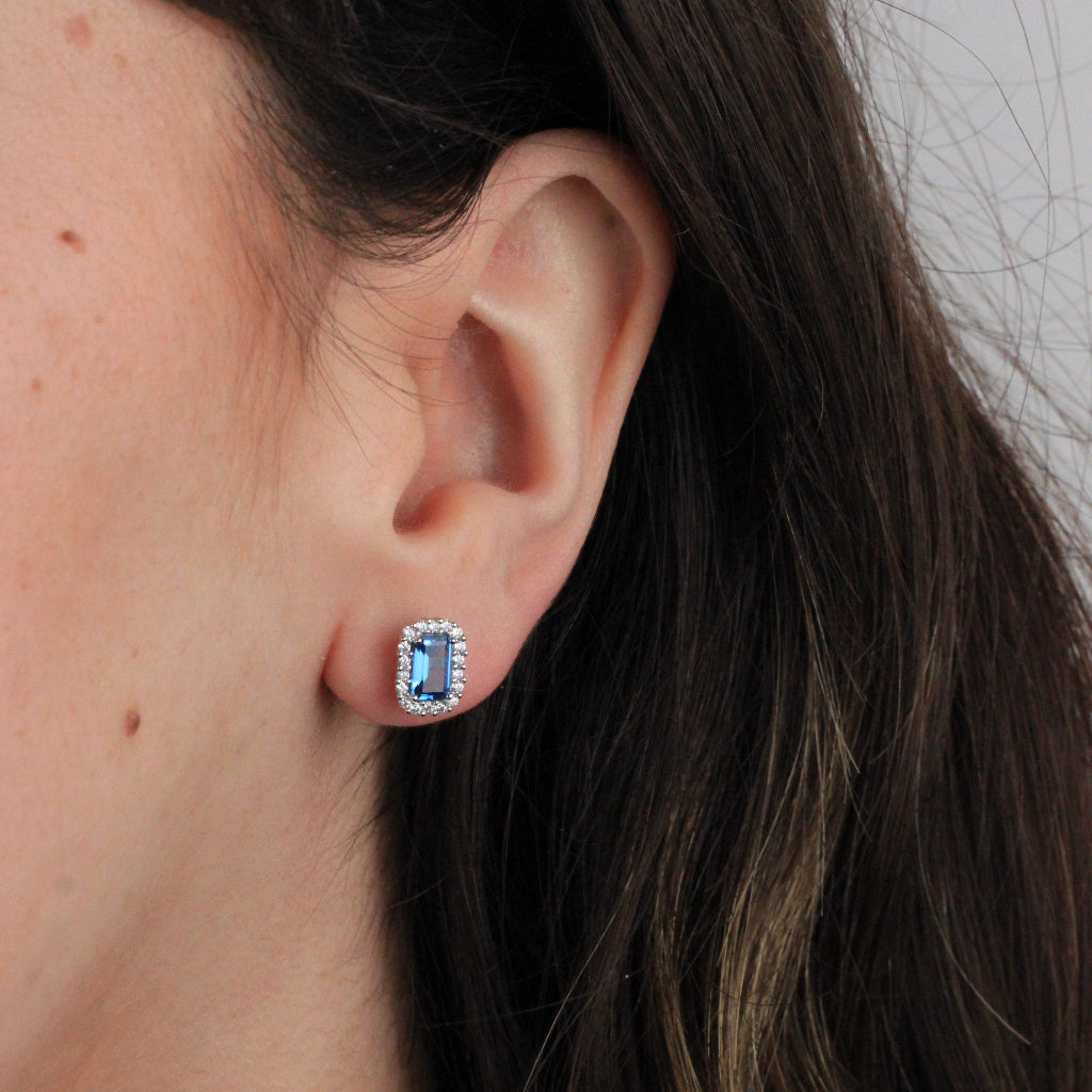 Pendientes de oro blanco de 18 quilates con una circonita azul con orla de circonitas incoloras.