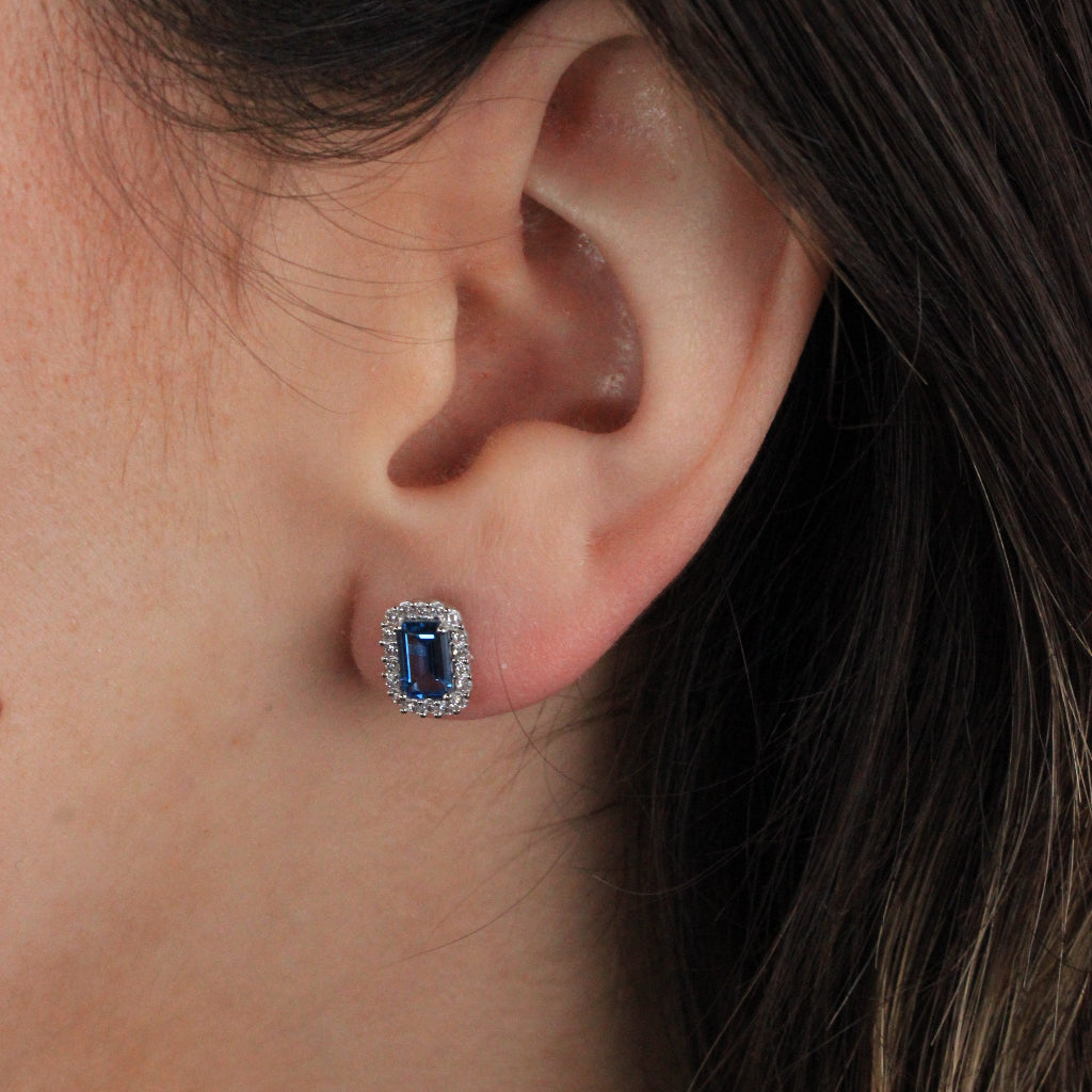 Pendientes de oro blanco de 18 quilates con una circonita azul con orla de circonitas incoloras.