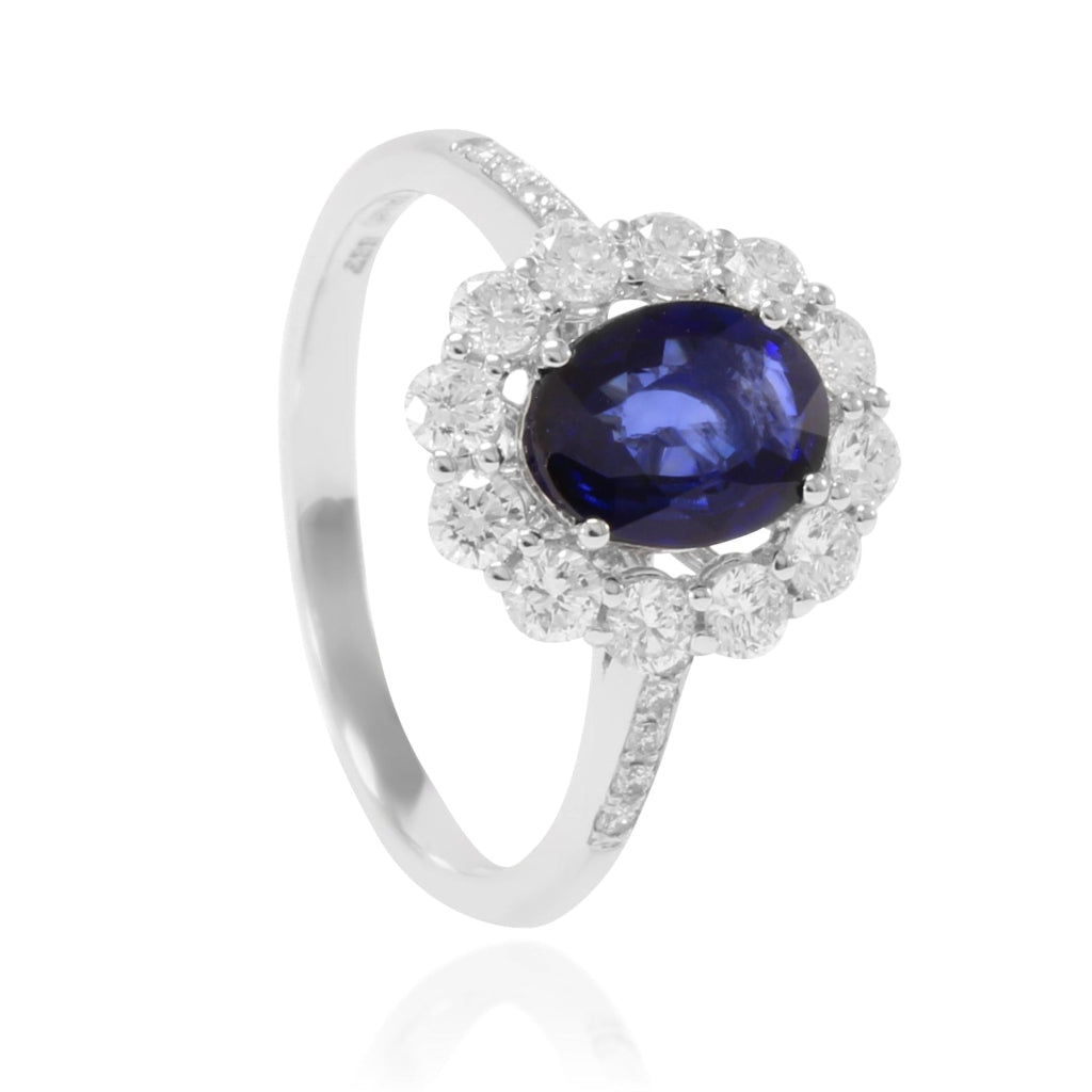 Anillo de oro blanco de 18k con zafiro oval y orla de diamantes y en los laterales