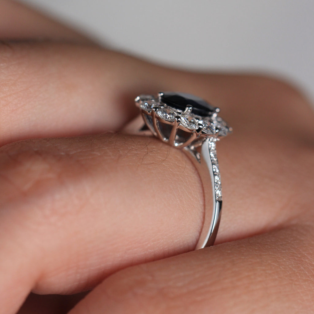 Anillo de oro blanco de 18k con zafiro oval y orla de diamantes y en los laterales