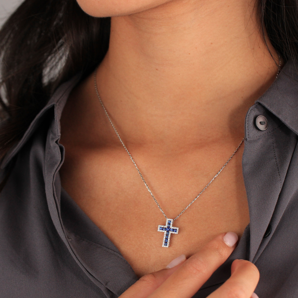 Gargantilla realizada en oro blanco de 18 quilates con un colgante de cruz con diamantes talla brillante con un peso total de 0,35cts y zafiros azules talla brillante.