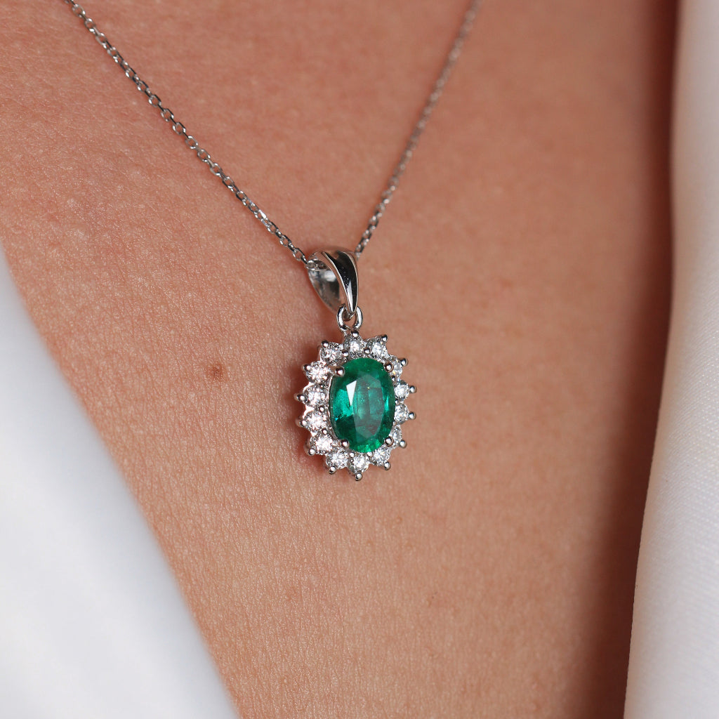 Colgante de oro blanco de 18k con esmeralda central y orla de diamantes