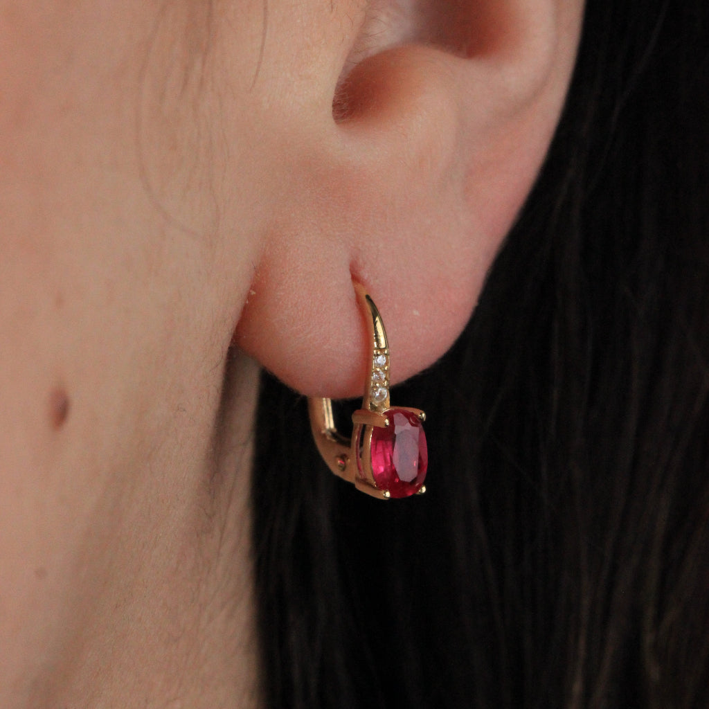 Pendientes en oro amarillo de 18 quilates con una rubí talla oval en garras y tres circonitas.